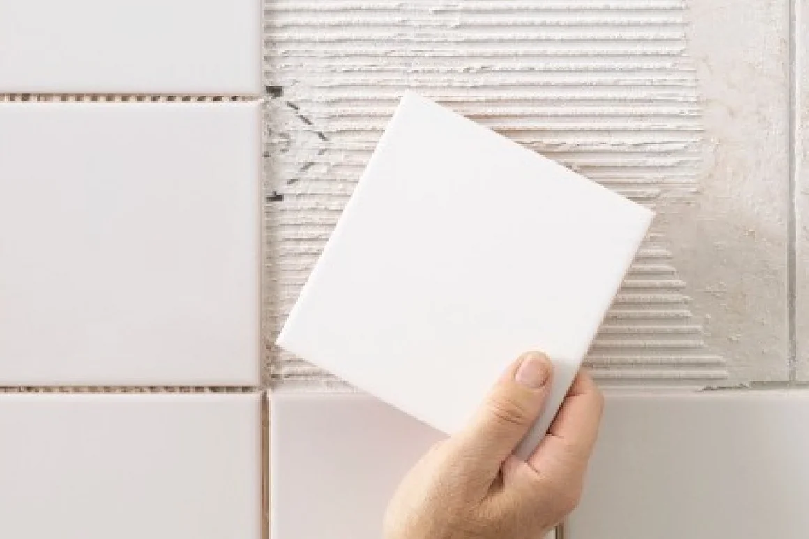 Hand hält Fliese vor Wand